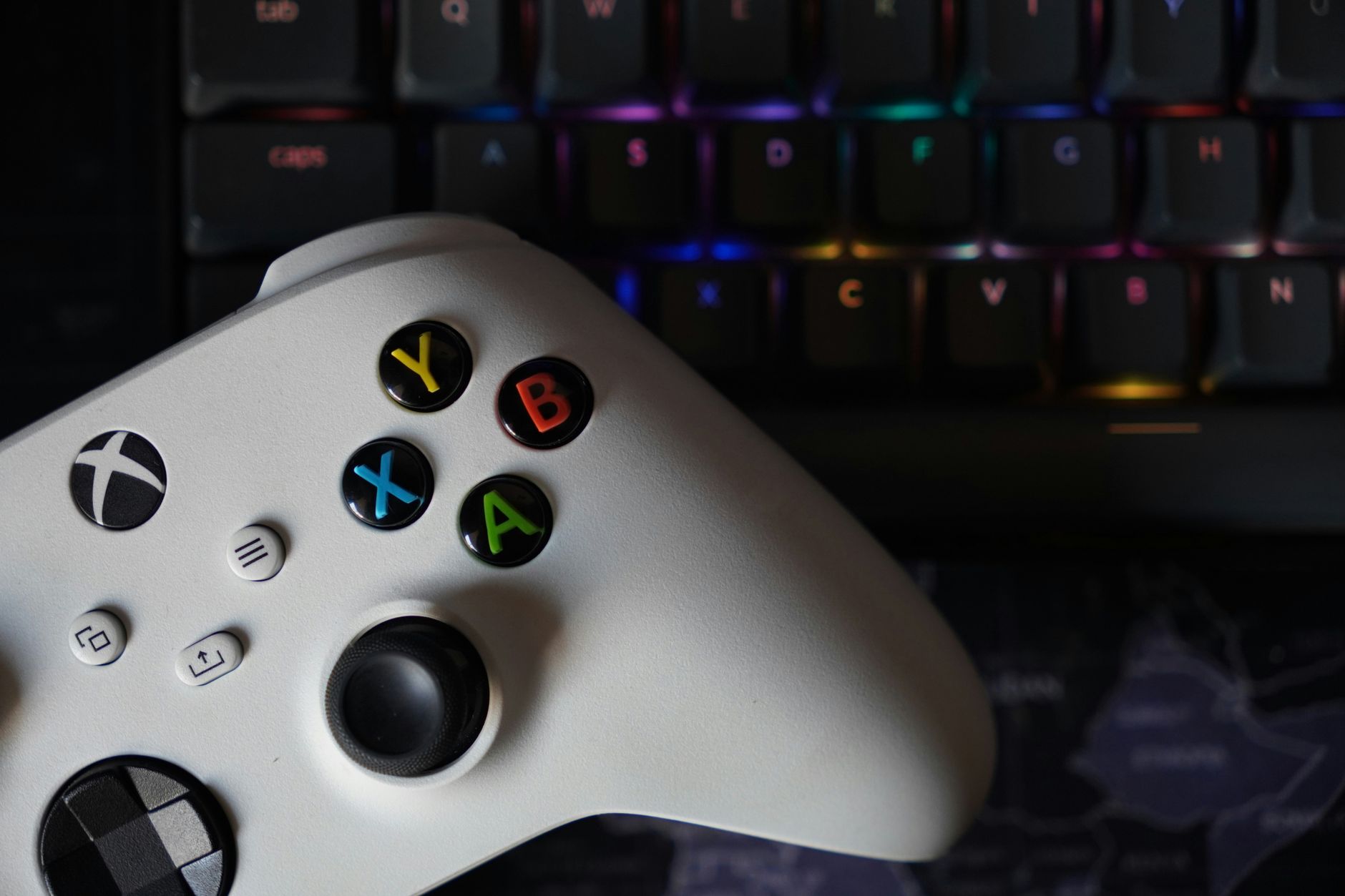Game controller beside illuminated RGB keyboard, highlighting technology and gaming equipment.