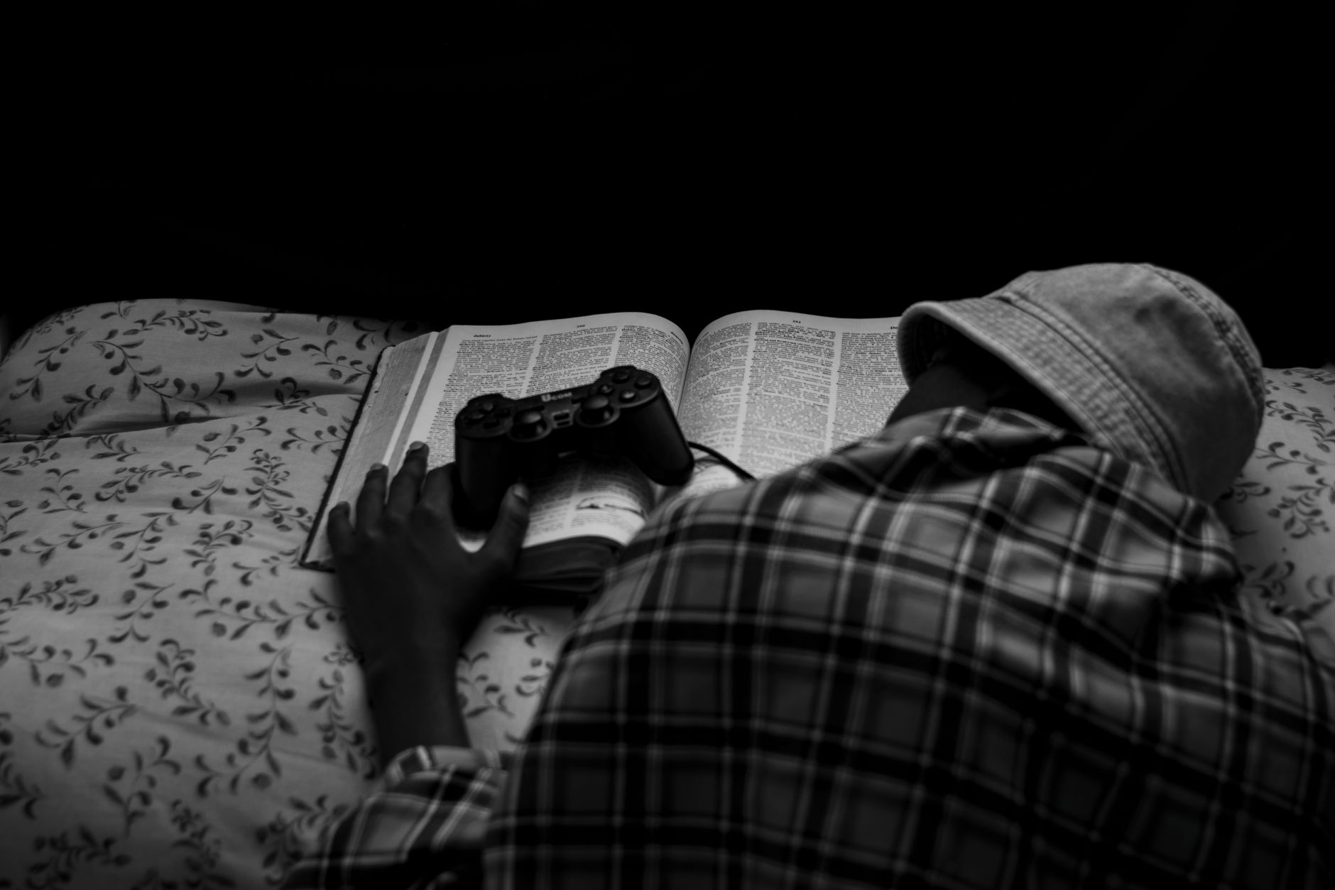 A person resting with a game controller on an open book, captured in monochrome.