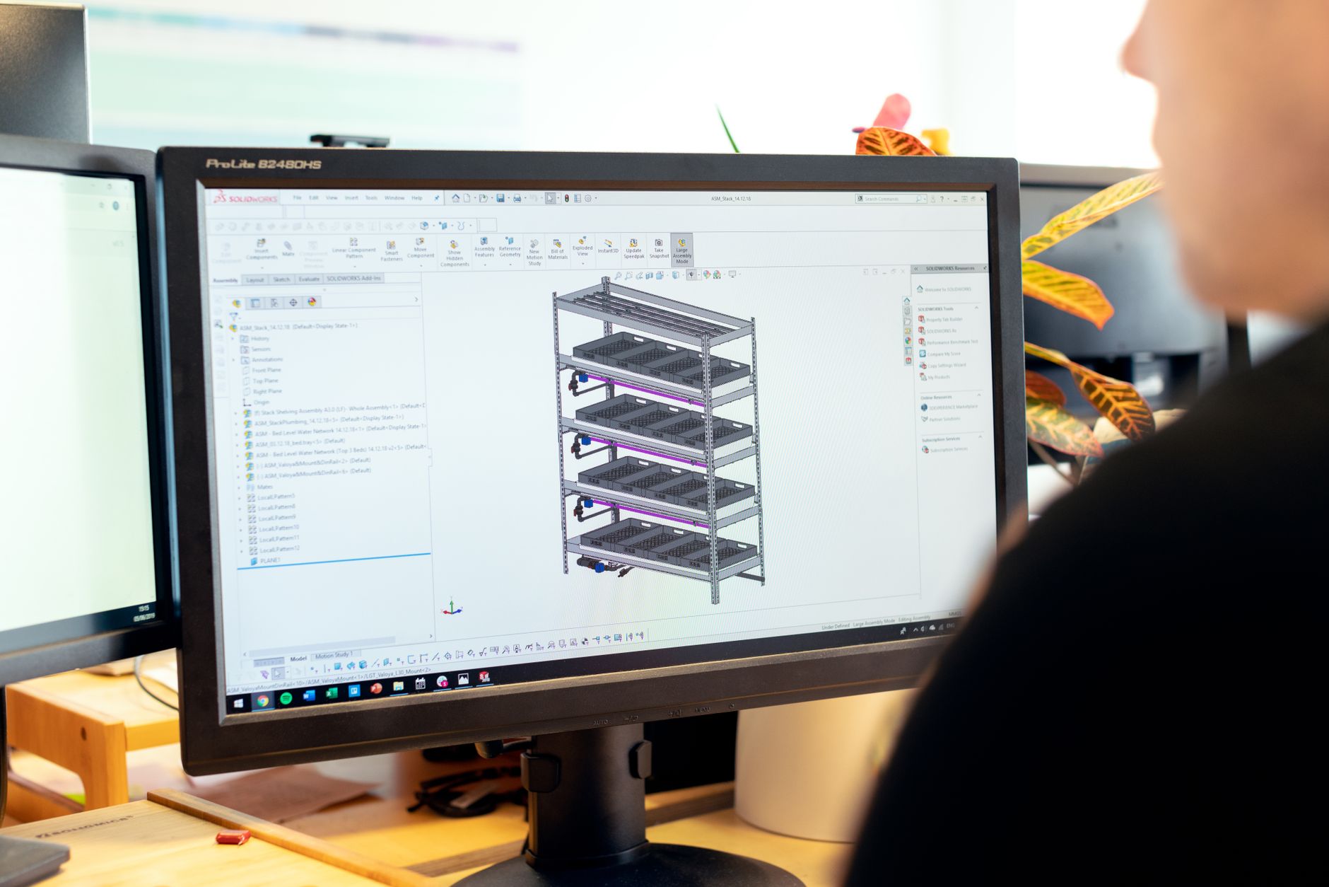 A person sitting at a desk viewing a 3D CAD design on a desktop computer screen.
